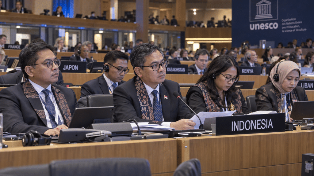 Delegasi diplomatik Indonesia duduk di meja sidang resmi UNESCO dengan papan nama kenegaraan dan dokumen ratifikasi.